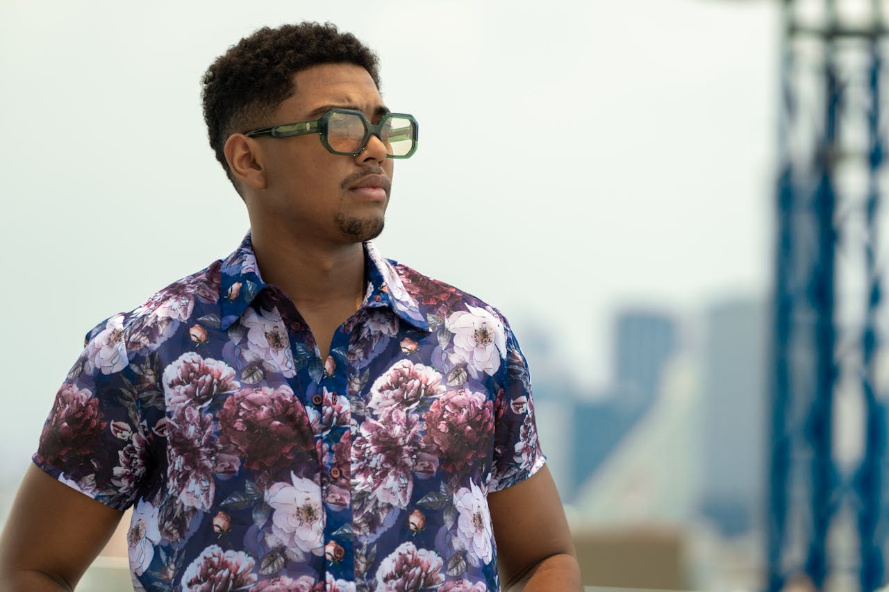 services-03 A fashionable man wearing a floral shirt and sunglasses, gazing confidently outdoors.